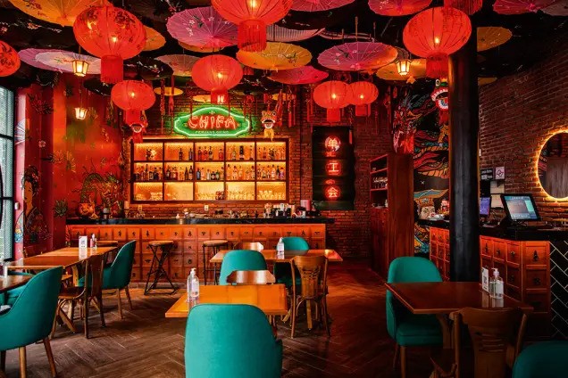 An Image of the chinese-themed restaurant with glowing red lanterns and bright emerald green seating contrasting the red lights.